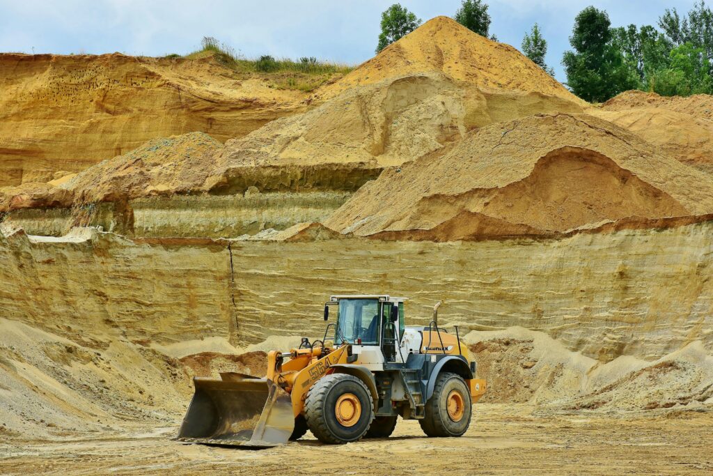 Mines An excavator working in an open pit mine surrounded by sandy terrain and clear sky.